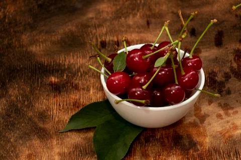 Red berries of a cherry in a white ceramic bowl. On a wooden background. A lo 库存照片
