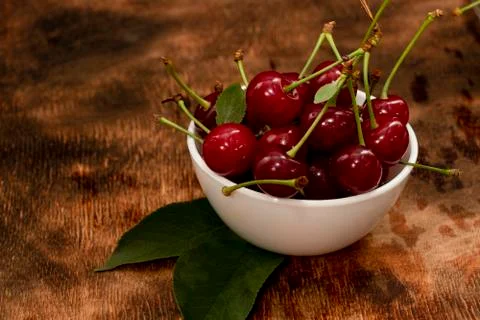 Red berries of a cherry in a white ceramic bowl. On a wooden background. A lo Stock Photos