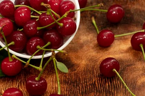 Red berries of a cherry in a white ceramic bowl. On a wooden background. A lo Stock Photos
