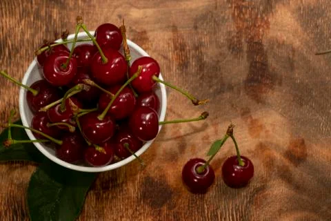 Red berries of a cherry in a white ceramic bowl. On a wooden background. A lo Stock Photos