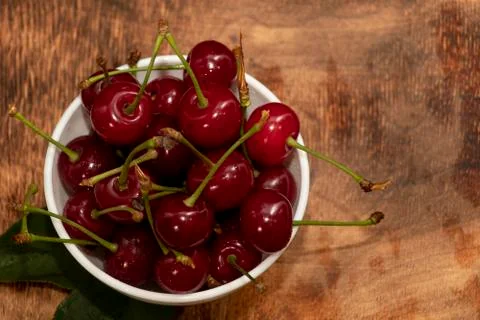 Red berries of a cherry in a white ceramic bowl. On a wooden background. A lo Stock Photos