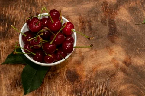 Red berries of a cherry in a white ceramic bowl. On a wooden background. A lo Stock Photos