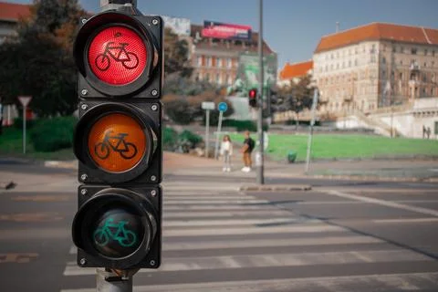 A red bicycle traffic light glows at a city crosswalk, with its amber and green Stock Photos