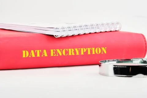 A red binder labeled data encryption rests on a surface alongside a silver bi Stock Photos