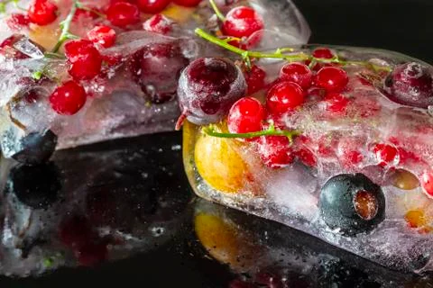 Red, black currant, berries and cherry plum frozen in ice, dark background Stock Photos