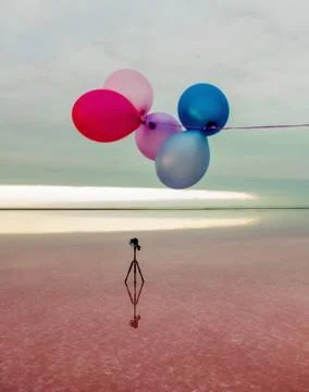 Red, blue, pink, blue balloons at sunrise on a pink salt lake and a tripod with Stock Photos