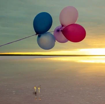 Red, blue, pink, blue balloons at sunrise on a pink salt lake and glasses of Stock Photos