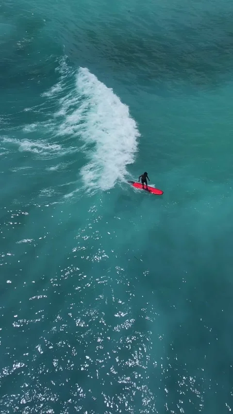 Red Board Slices Through Ocean Water. Sunlit Spray Erupts As Surfer Maneuvers 库存影片 335327003