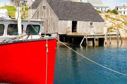 Red boat in foreground of rustic building on water in fishing village Stock Photos