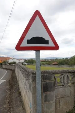 A red-bordered triangular speed bump warning sign stands next to a stone wa.. Foto stock
