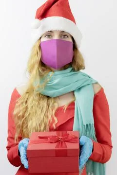 Red box with a gift in the hands of a lady Santa dressed in a medical mask and Stock Photos
