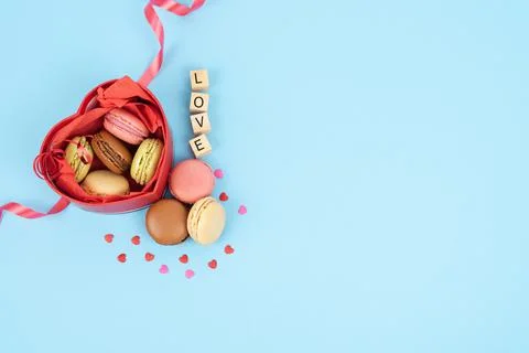 Red box in the shape of an open heart full of macaroons on a blue background. Stock Photos