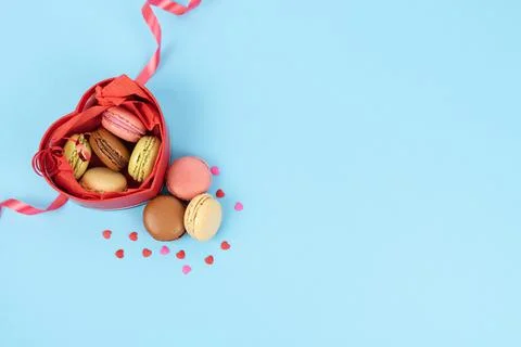 Red box in the shape of an open heart full of macaroons on a blue background. Stock Photos