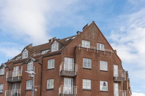 Red brick apartment building with balconies and dormer windows under blue sky Stock Photos
