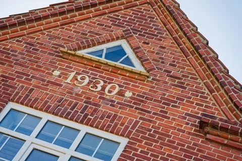 Red brick building facade with triangular window and year 1930 inscription 스톡 사진