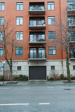 A red brick building has multiple balconies on its front, while the road in f Stockfoto's
