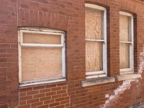 A red brick façade with three weathered white-framed windows Stock Photos