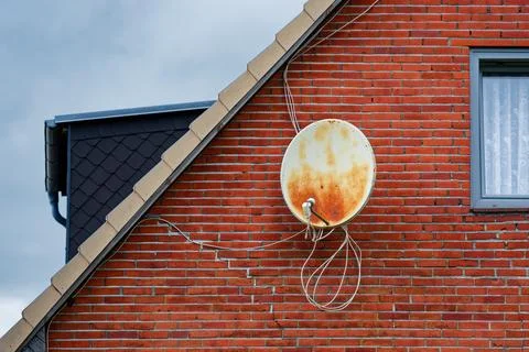 Red brick house with rusty white satellite dish on wall Stock Photos