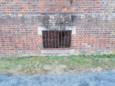 Red brick masonry building with window bars and grass Stock Photos