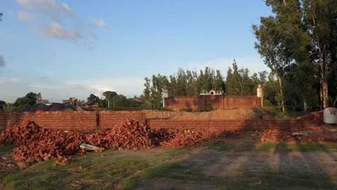 Red brick wall construction site with building materials in an open field 스톡 동영상 347256697