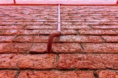 Red brick wall surface with a flexible electrical conduit pipe Foto stock
