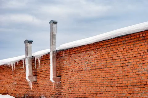 Red brick wall with ventilation pipes atop a concrete fence adorned with icic Stock Photos