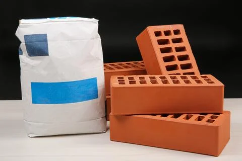 Red bricks and bag of cement on light wooden table against black background.. Foto stock