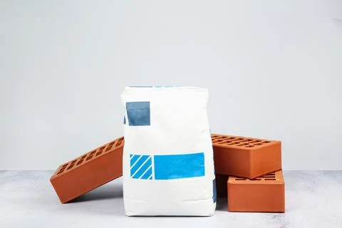 Red bricks and bag of cement on textured table against light background. Bu.. Foto stock