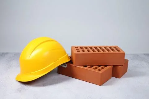 Red bricks and hard hat on textured table against light background Stock Photos
