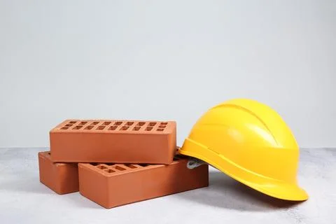Red bricks and hard hat on textured table against light background Stock Photos