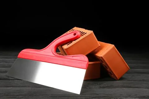 Red bricks and putty knife on wooden table. Building material Stock Photos