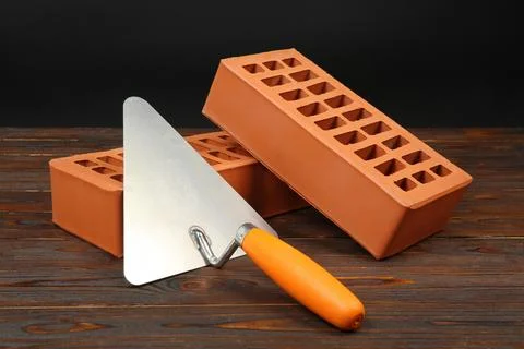 Red bricks and putty knife on wooden table. Building material Stock Photos