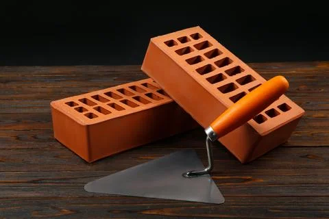 Red bricks and putty knife on wooden table. Building material Stock Photos