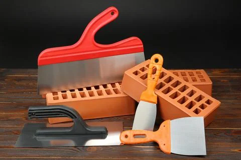 Red bricks and putty knives on wooden table. Building material and construc.. Stock Photos