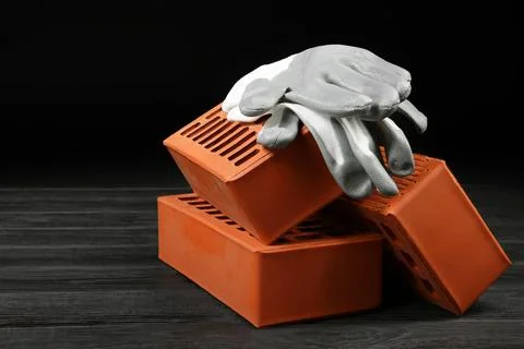 Red bricks and rubber gloves on wooden table. Building material Stock Photos