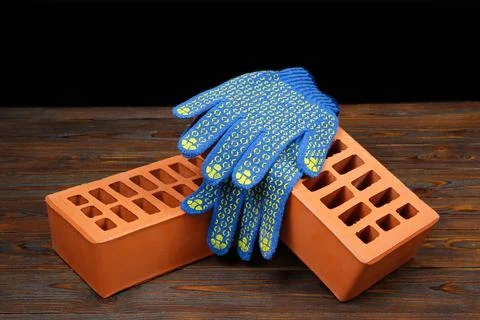 Red bricks and rubber gloves on wooden table. Building material Stock Photos