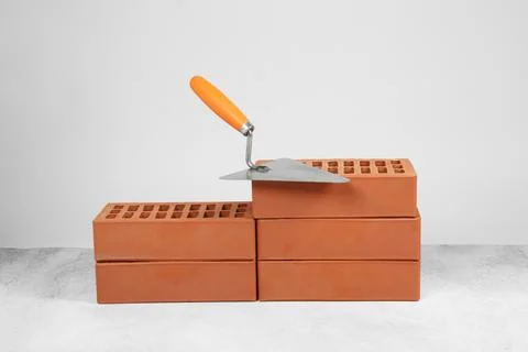 Red bricks and trowel on textured table against light background. Building .. Stock Photos