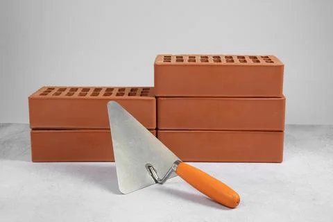 Red bricks and trowel on textured table against light background. Building .. Stock Photos