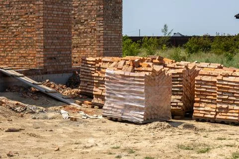 Red bricks are stacked on the ground near a brick house under construction... Stockfoto's