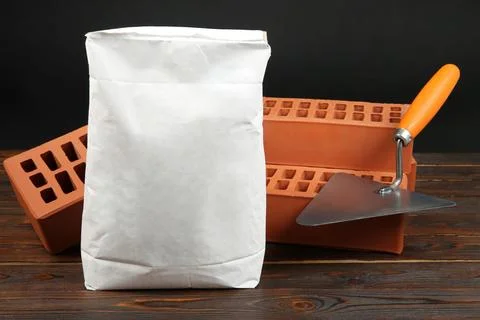 Red bricks, bag of cement powder and putty knife on wooden table. Building .. Stock Photos
