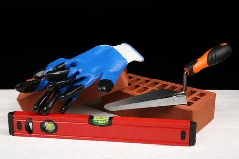 Red bricks, building level, gloves and trowel on white wooden table. Constr.. Stock Photos