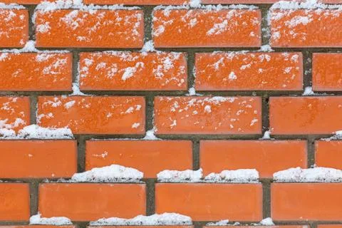Red bricks form a sturdy wall. Snow lightly dusts the surface. Stock Photos