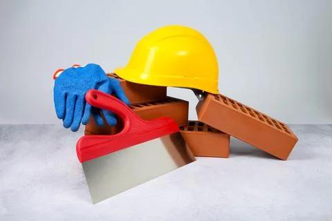 Red bricks, plastering trowel, gloves and hardhat on textured table against.. Stock Photos