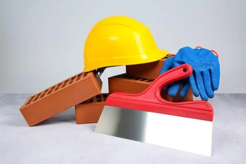 Red bricks, plastering trowel, gloves and hardhat on textured table against.. Stock Photos