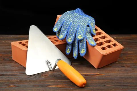 Red bricks, putty knife and rubber gloves on wooden table. Building material Stock Photos