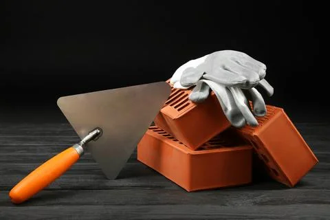 Red bricks, putty knife and rubber gloves on wooden table. Building material Stock Photos