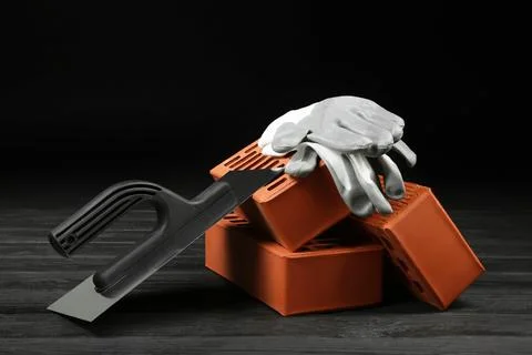 Red bricks, putty knife and rubber gloves on wooden table. Building material Stock Photos