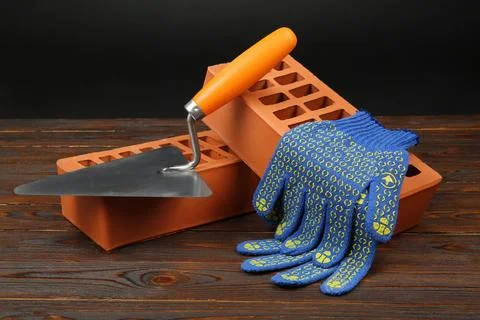 Red bricks, putty knife and rubber gloves on wooden table. Building material Stock Photos