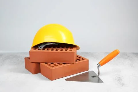 Red bricks, trowel and hard hat on textured table against light background Stock Photos
