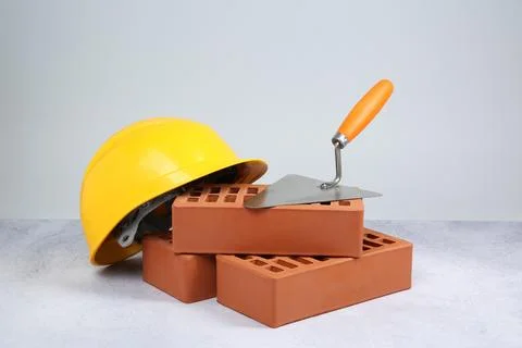 Red bricks, trowel and hard hat on textured table against light background 库存照片